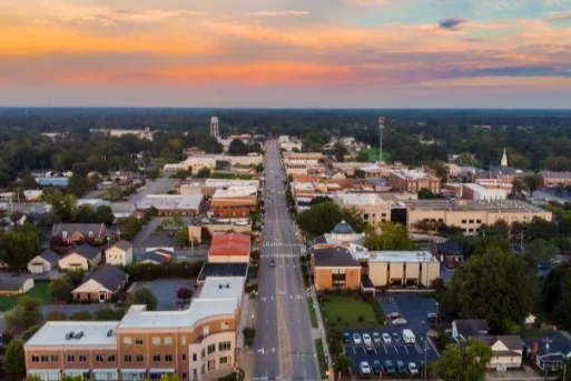 Small Town Main Street from Above Aerial view of a small town's main street at sunset, with buildings, trees, and a water tower in the distance.