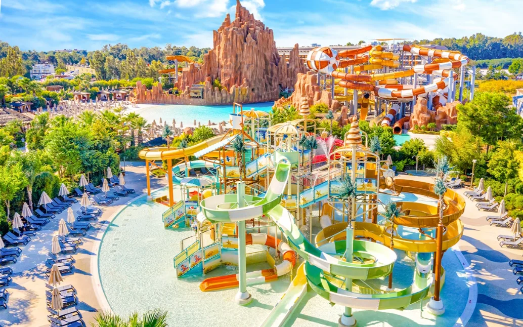 Vibrant Water Park Adventure Expansive water park with numerous colorful slides, pools, and a large artificial rock mountain feature under a sunny sky.