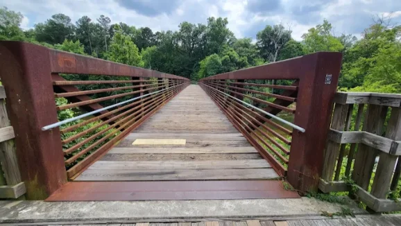 Woodland Pedestrian Bridge View looking across a wooden pedestrian bridge with weathered steel railings, surrounded by green trees.