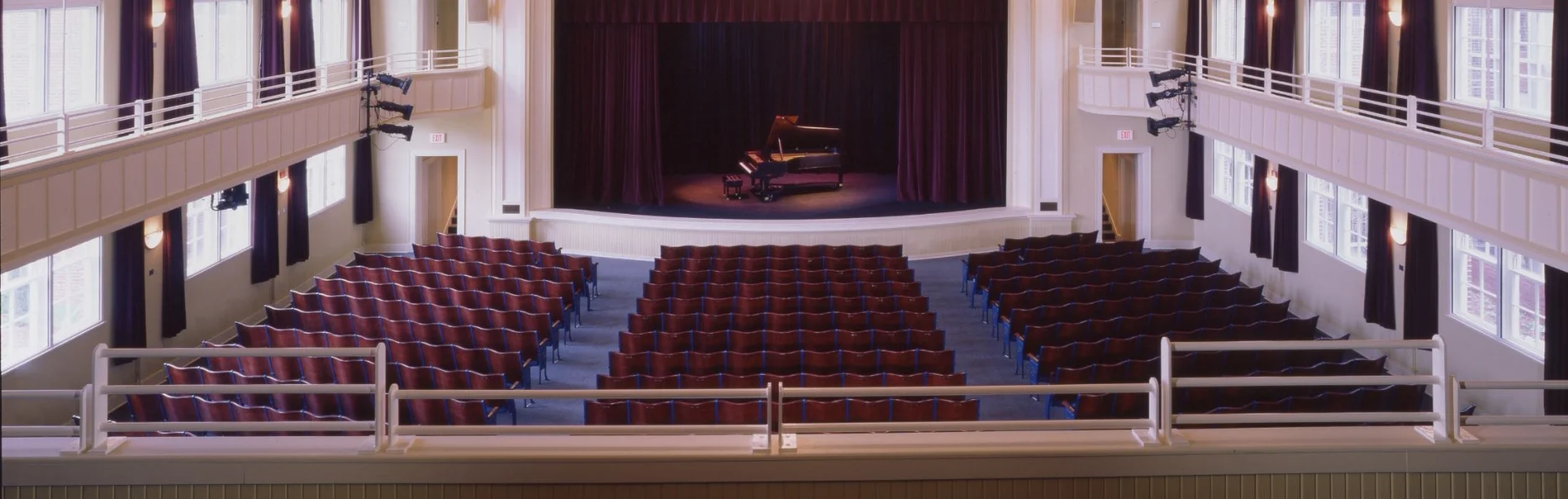 Classic Auditorium Interior Interior view of an empty auditorium with red seats, a stage with a grand piano, and balconies.